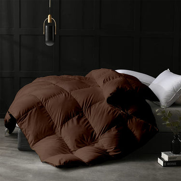 Brown quilt on a bed in a darkly decorated room with a lamp and books.