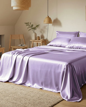 Purple satin bedding set on a bed in a bedroom with wooden furniture and decor.