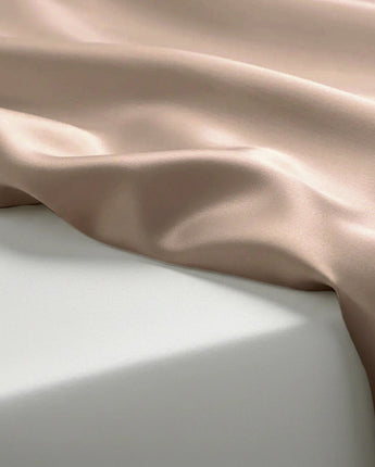 Silky fabric with a soft pinkish-beige color draped over a light gray surface.