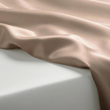 Silky fabric with a soft pinkish-beige color draped over a light gray surface.