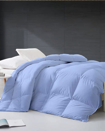 Blue comforter on a bed in a room with a dark wall and small table.