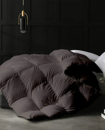 Dark gray quilt on a bed in a dimly lit room with a black wall and white pillows.