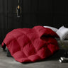 Red quilted comforter on a bed in a darkly decorated room.